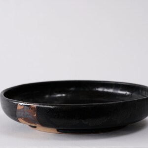 stunning handmade stoneware low serving bowl with a soft contemporary curve leading to the elevating foot ring. The bowl is finished in a metallic textured black glaze with a ray of unglazed part in the center.