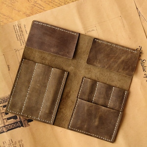 May include: A brown leather organizer featuring two horizontal top pockets and two lower sections, each divided into three vertical slots. The leather has a matte, distressed finish with visible white stitching along the edges of all pockets.