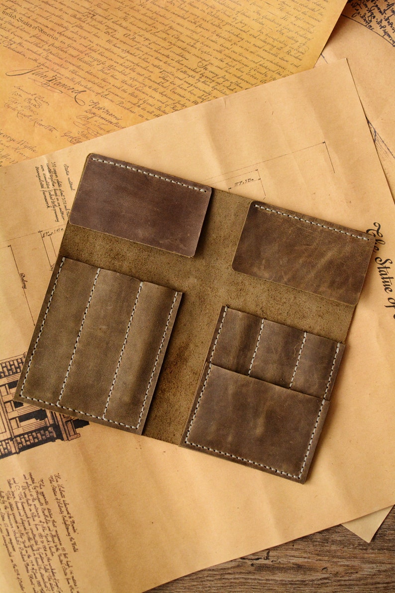 May include: A brown leather organizer featuring two horizontal top pockets and two lower sections, each divided into three vertical slots. The leather has a matte, distressed finish with visible white stitching along the edges of all pockets.