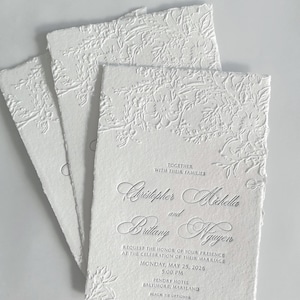 May include: Three white rectangular wedding invitations with deckled edges and embossed floral patterns. The text reads: Together with their families, Christopher Michella and Brittany Nguyen request the honor of your presence at the celebration of their marriage, Monday, May 25, 2026, 5:00 PM, Pendry Hotel, Baltimore, Maryland, Black Tie Optional.
