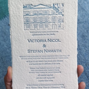 May include: Cream-colored wedding invitation with blue text and a detailed illustration of a building. The invitation includes the names Victoria Nicol & Stefan Namath, along with the date and time of the ceremony.
