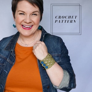 May include: A woman wearing a denim jacket and orange shirt smiles, showcasing a crocheted cuff bracelet. The olive green cuff features a geometric pattern and is adorned with three blue buttons. The text "CROCHET PATTERN" is displayed in a black frame.
