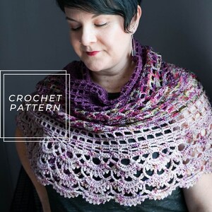 Puede incluir: Un patrón de chal de ganchillo con un degradado de color morado, rosa y blanco. El patrón presenta un delicado diseño de encaje con un borde festoneado.