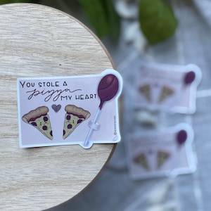 May include: A pink and white sticker with a cartoon pizza slice and a lollipop. The sticker says "You stole a pizza my heart".