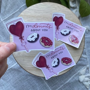 May include: Three pink and white stickers with a heart-shaped balloon and two donuts. The text on the stickers reads "I'm donuts about you".