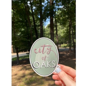 May include: A green and white oval sticker with the text "city of oaks" in pink cursive lettering.