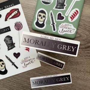 May include: Three stickers with the text "I like my men morally grey" in black and white text on a gradient background. The stickers are on a wooden surface.