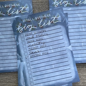 May include: A blue and white checklist with the text "SMALL BUSINESS big list" at the top. The checklist includes items such as "print stickers", "pack orders", "order boxes", "inventory", "market prep", "taxes", and "notepad pics".