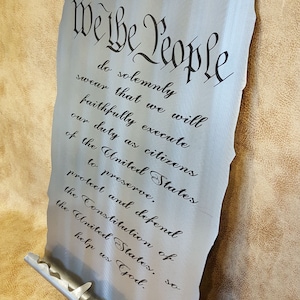 May include: A metal scroll with the text "We the People" and the first few lines of the Preamble to the United States Constitution. The scroll is silver and has a textured surface.