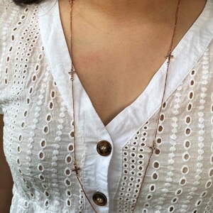 May include: A rose gold chain necklace with small cross charms. The crosses are set with black stones.