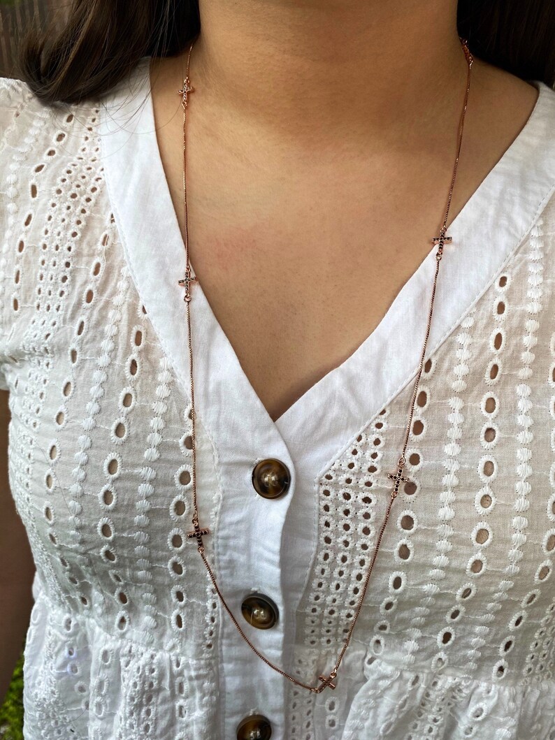 May include: A rose gold chain necklace with small cross charms. The crosses are set with black stones.