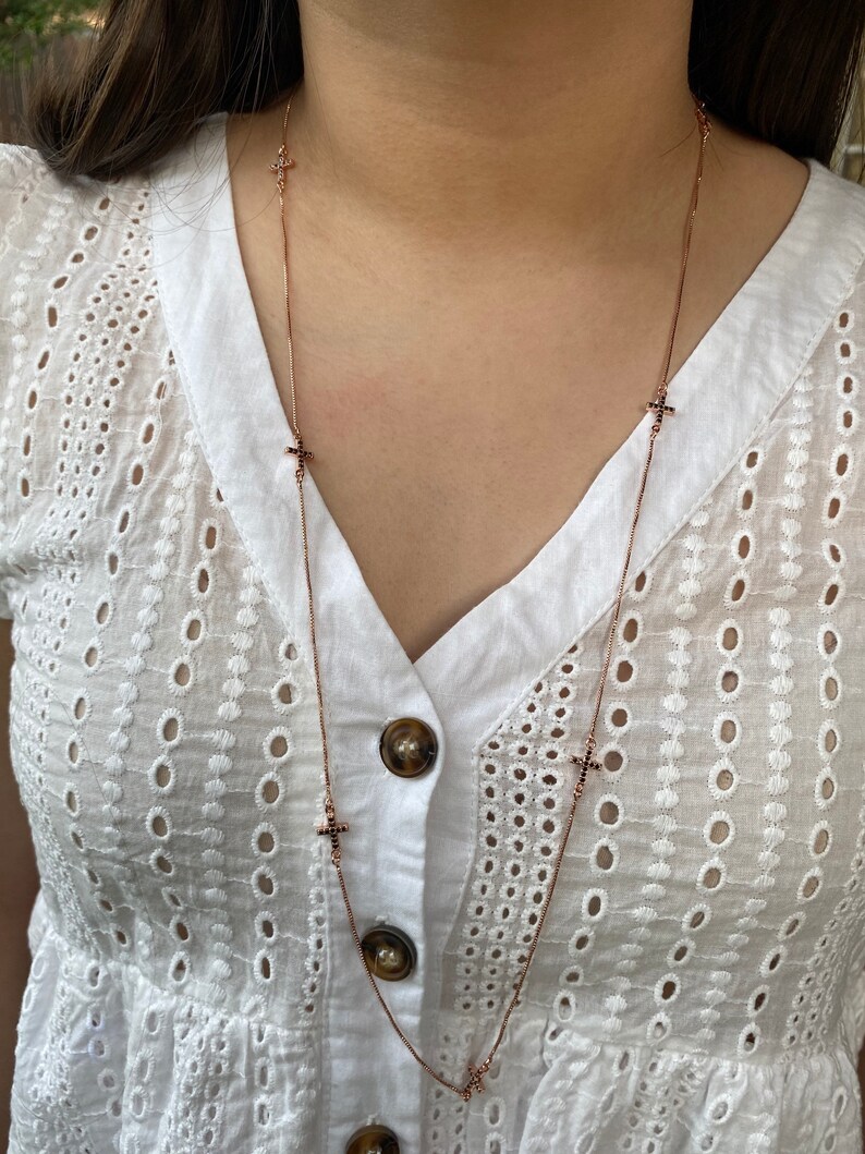 May include: A rose gold chain necklace with small black cross charms. The necklace is layered and has multiple cross charms.