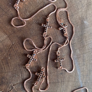 May include: A rose gold chain necklace with multiple black cross pendants adorned with small black crystals.