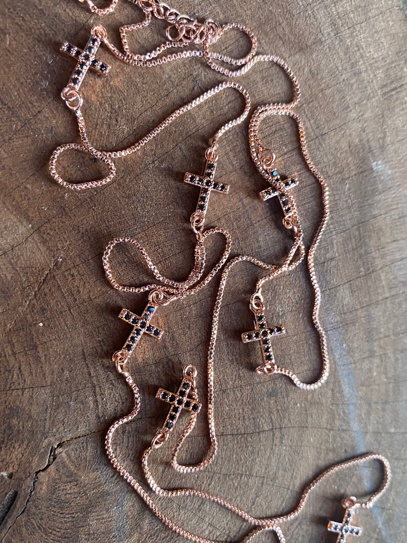May include: A rose gold chain necklace with multiple black cross pendants adorned with small black crystals.