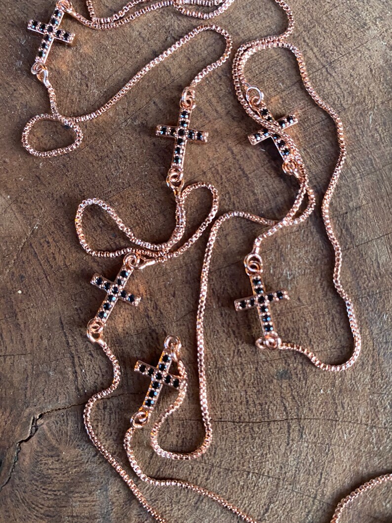 May include: Multiple rose gold chains with black crystal cross pendants. The chains are layered and the crosses are of varying sizes.