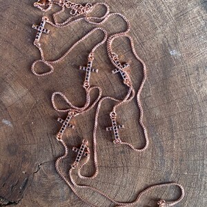 May include: A rose gold chain necklace with multiple black crystal cross pendants. The necklace is layered and has a delicate chain.