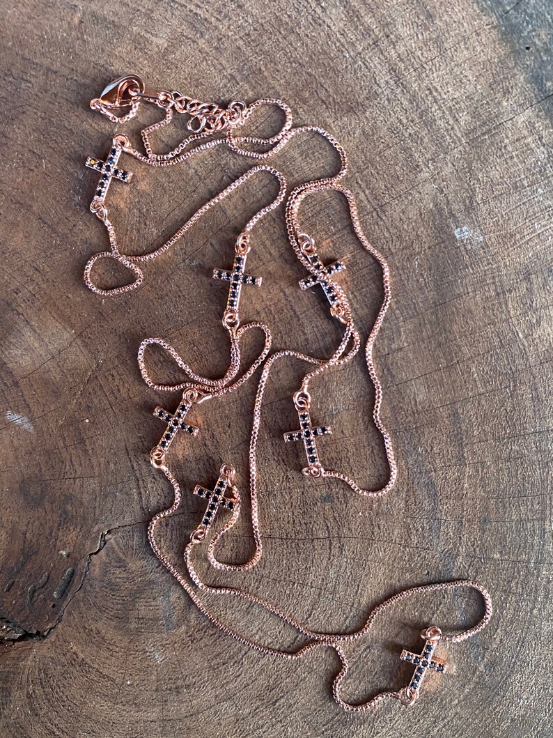 May include: A rose gold chain necklace with multiple black crystal cross pendants. The necklace is layered and has a delicate chain.