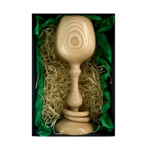 Top view of a Magill Woodcraft Ireland wooden Irish wedding goblet, nestled in a black cardboard gift box. There is light colored wood wool and green tissue paper as packaging in the box. The wooden goblet has two captive rings around its stem.