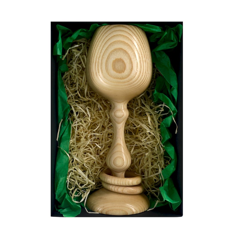 Top view of a Magill Woodcraft Ireland wooden Irish wedding goblet, nestled in a black cardboard gift box. There is light colored wood wool and green tissue paper as packaging in the box. The wooden goblet has two captive rings around its stem.
