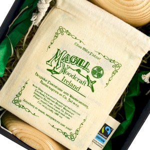 Close up of a screen printed, Fair trade drawstring organic cotton bag, in a black cardboard gift box, beside a wooden traditional Irish wedding goblet. A Magill Woodcraft Ireland logo and Celtic leaf corners are printed in green colour.