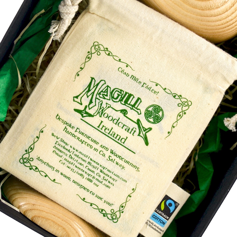 Close up of a screen printed, Fair trade drawstring organic cotton bag, in a black cardboard gift box, beside a wooden traditional Irish wedding goblet. A Magill Woodcraft Ireland logo and Celtic leaf corners are printed in green colour.