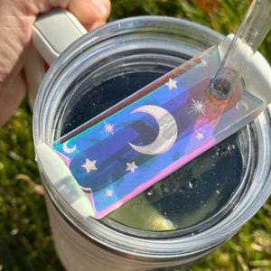 May include: A clear tumbler with a lid and a straw. The lid has a holographic sticker with a crescent moon and stars.