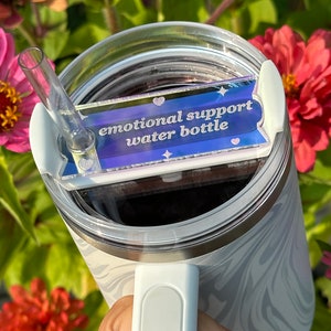 May include: White stainless steel water bottle with a marble pattern and a clear lid. The bottle has a white handle and a clear straw. A sticker on the bottle reads "emotional support water bottle" with a blue, purple, and pink gradient background.
