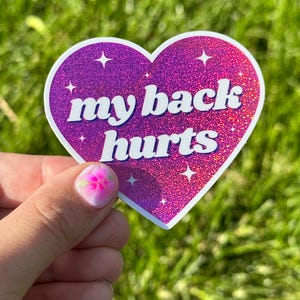 May include: Pink heart-shaped sticker with glitter and the text "my back hurts" in white letters.