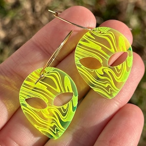 May include: A pair of neon green alien head hoop earrings with a swirling pattern. The earrings are made of acrylic and have gold hoops.