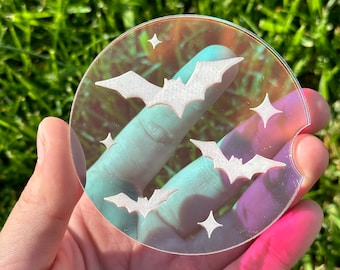 May include: A clear iridescent round coaster with a white bat design and white star accents.
