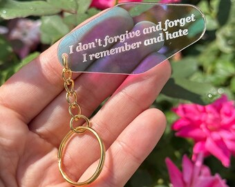May include: A iridescent keychain with a gold chain and ring. The keychain features a clear acrylic tag with the text "I don't forgive and forget I remember and hate".