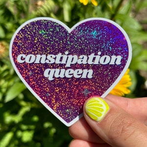 May include: A heart-shaped sticker with a glittery purple background and white text that reads "constipation queen".