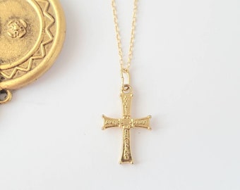 May include: A gold chain necklace with a small gold cross pendant. The cross has intricate details and lettering.