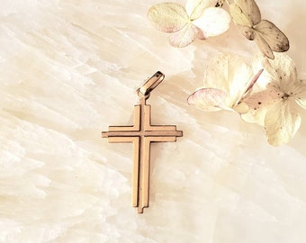 May include: A gold-toned cross pendant with a simple, elegant design. The cross has a slightly textured surface and is made of metal.
