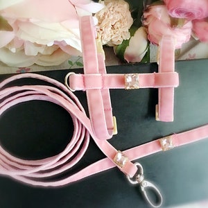 May include: Pink velvet dog harness and leash set with crystal embellishments. The harness has a D-ring for attaching a leash. The leash has a clip for attaching to a collar.