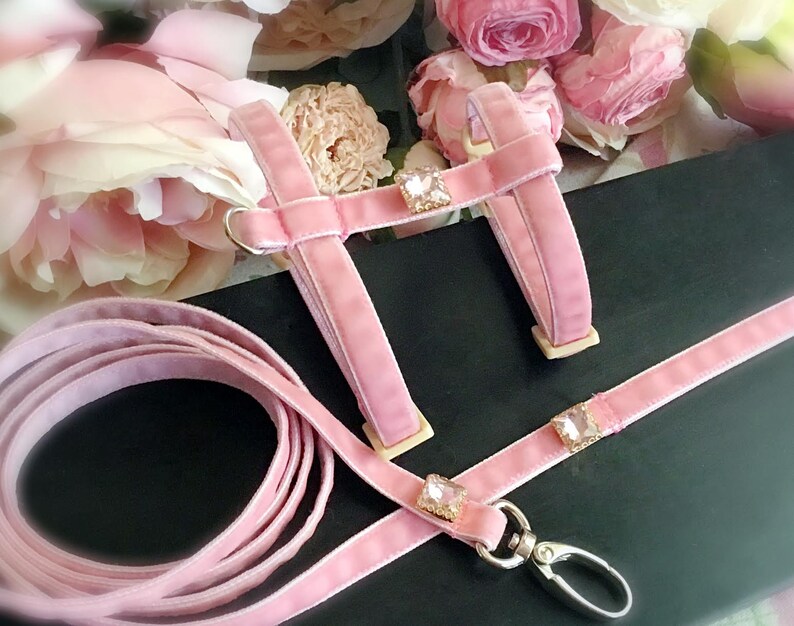 May include: Pink velvet dog harness and leash set with crystal embellishments. The harness has a  adjustable chest strap and the leash has a metal clip.