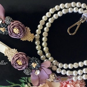 May include: A white leather leash and a pearl necklace with a silver clasp. Both are adorned with purple, gold, and gray fabric flowers.