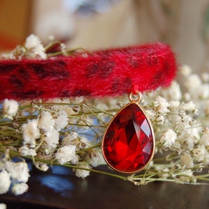May include: A red faux fur collar with a large, teardrop-shaped red rhinestone pendant.