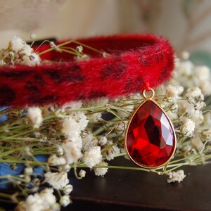 May include: A red faux fur choker with a leopard print pattern and a dangling red gemstone pendant.