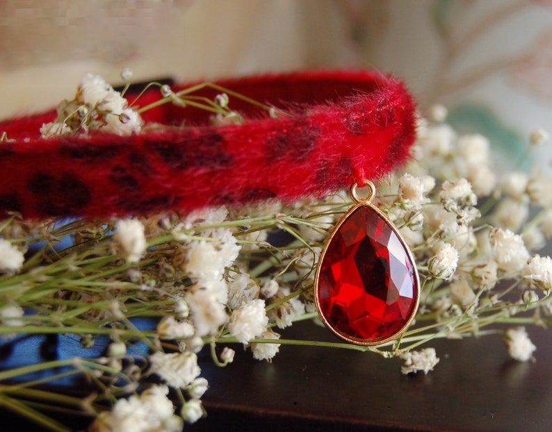 May include: A red faux fur choker with a leopard print pattern and a dangling red gemstone pendant.