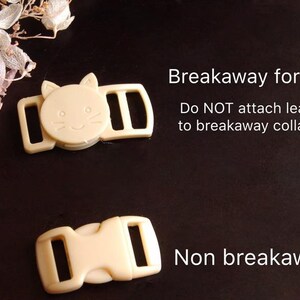 May include: Two beige plastic cat collar buckles. The top buckle has a cat face design and the text "Breakaway for cat. Do NOT attach leash to breakaway collar!" The bottom buckle has the text "Non breakaway".