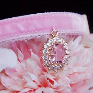 May include: A pink velvet cat collar with a gold pendant featuring a large oval-shaped pink gemstone surrounded by clear rhinestones.