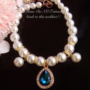K&ouml;nnte beinhalten: Eine wei&szlig;e Perlenkette mit einer goldenen Kette und einem tropfenf&ouml;rmigen Anh&auml;nger mit einem blauen Edelstein. Die Kette tr&auml;gt ein Schild mit der Aufschrift "Bitte KEINE Leine an diese Kette befestigen!"