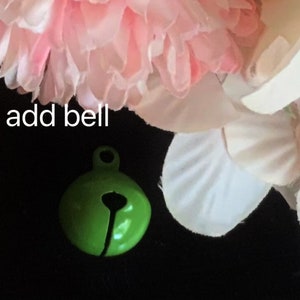 May include: A small green bell with a silver loop. The bell is on a black background with pink and white flowers.