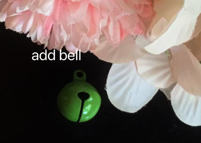 May include: A small green bell with a silver loop. The bell is on a black background with pink and white flowers.