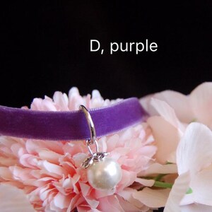 May include: Purple velvet choker with a silver charm and a white pearl pendant. The choker is displayed on a bed of pink flowers.  D, purple.