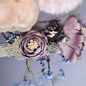 May include: A delicate white lace collar with a purple flower and a small green flower embellishment. The collar is decorated with a small crystal and a black flower.