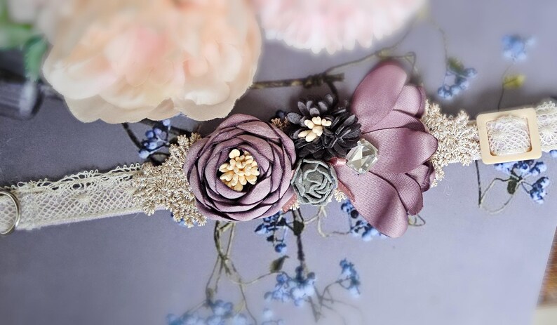 May include: A delicate white lace collar with a purple flower and a small green flower embellishment. The collar is decorated with a small crystal and a black flower.