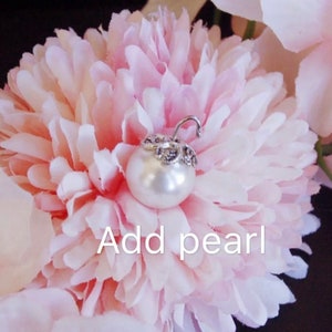 May include: A white pearl with a silver setting is placed on a pink flower. The text "Add pearl" is written below the pearl.