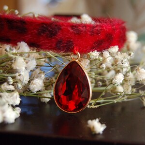 May include: A red faux fur collar with a large, teardrop-shaped, red gemstone pendant.
